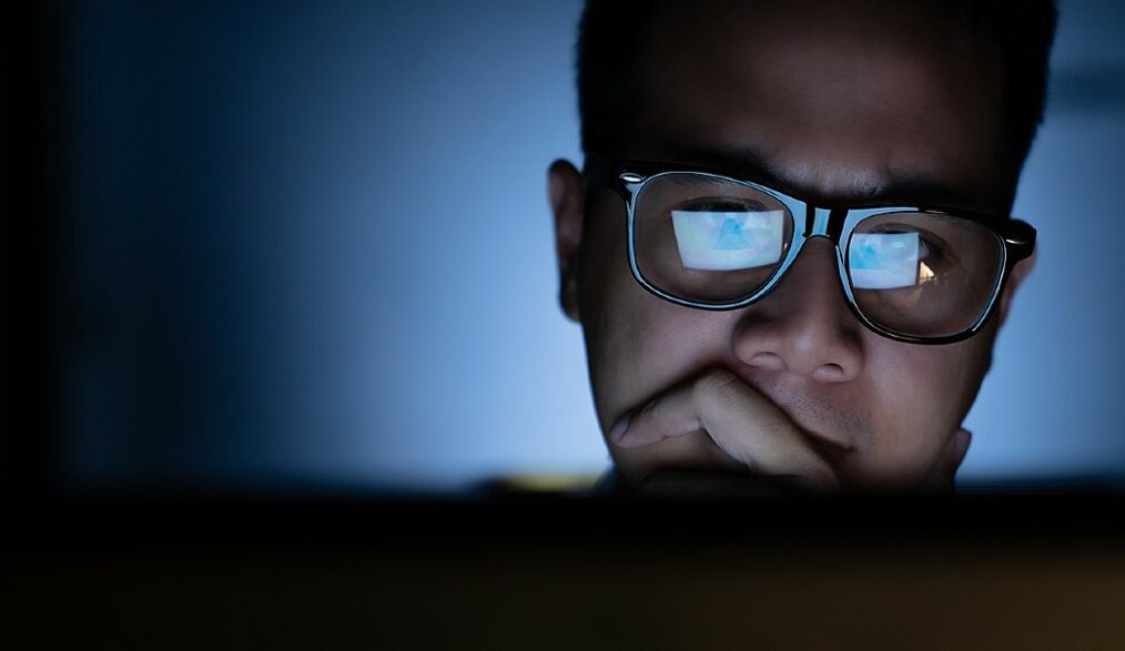homem olha para tela do computador em sala escura