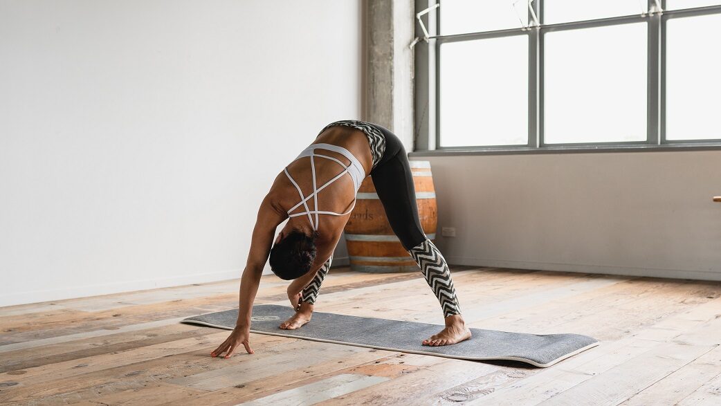 Mulher realiza yoga dentro de uma sala fecha e em um tapete específico para a prática
