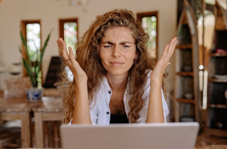 mulher de cabelos compridos levanta os braços perto do rosto como reação a uma mensagem no computador