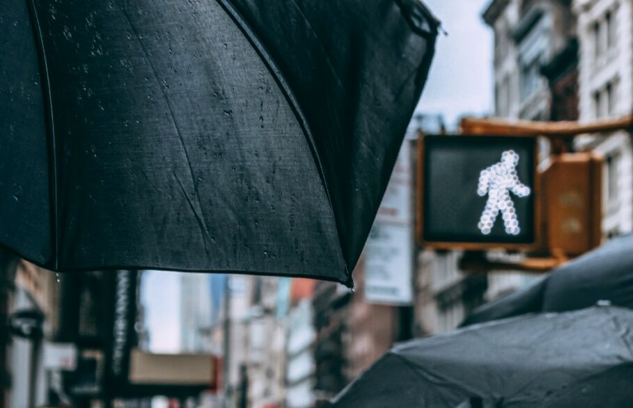 guarda-chuva se destaca na multidão em dia de chuva com sinal para atravessar a rua ao fundo