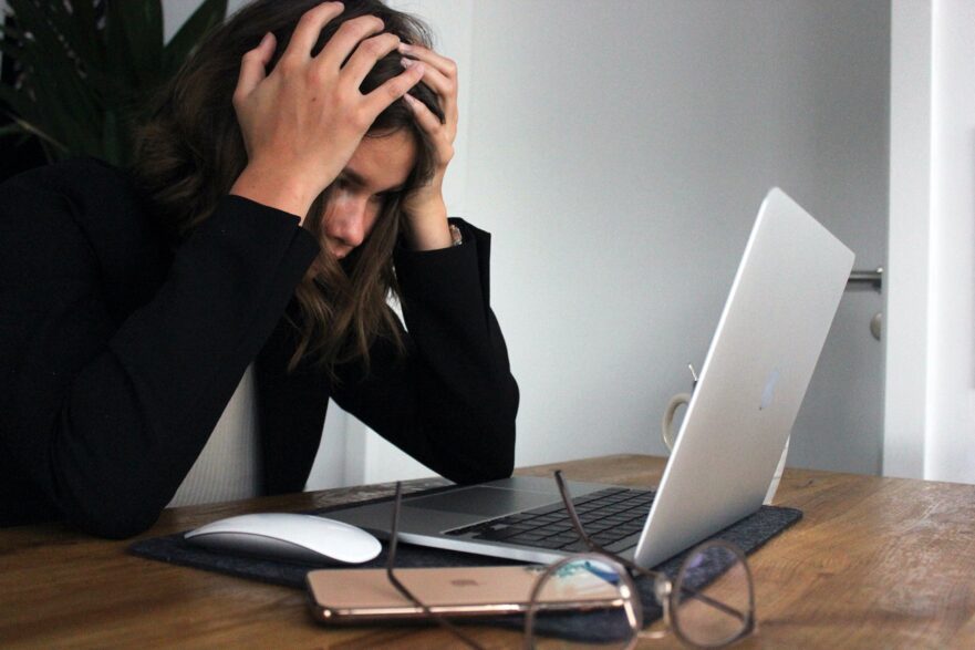 Imagem mostra uma mulher na frente do computador com as mãos na cabeça demonstrando estresse