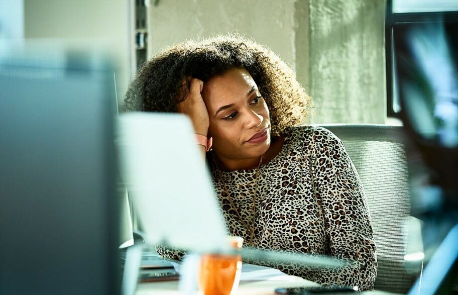 mulher negra olha preocupada para o lado tendo computador à sua frente