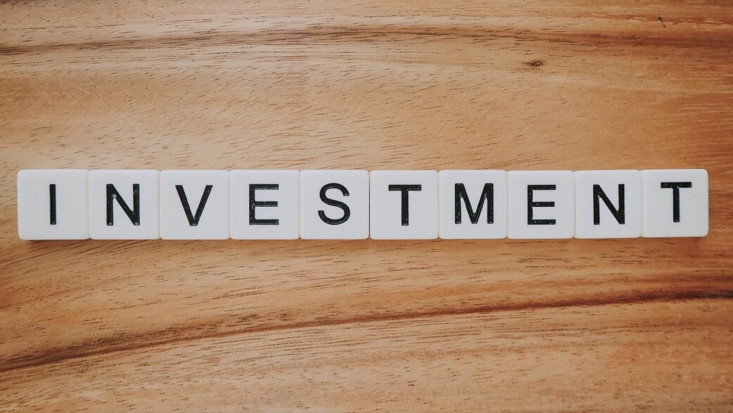 Imagem mostra blocos brancos em um fundo de madeira formando a palavra investment