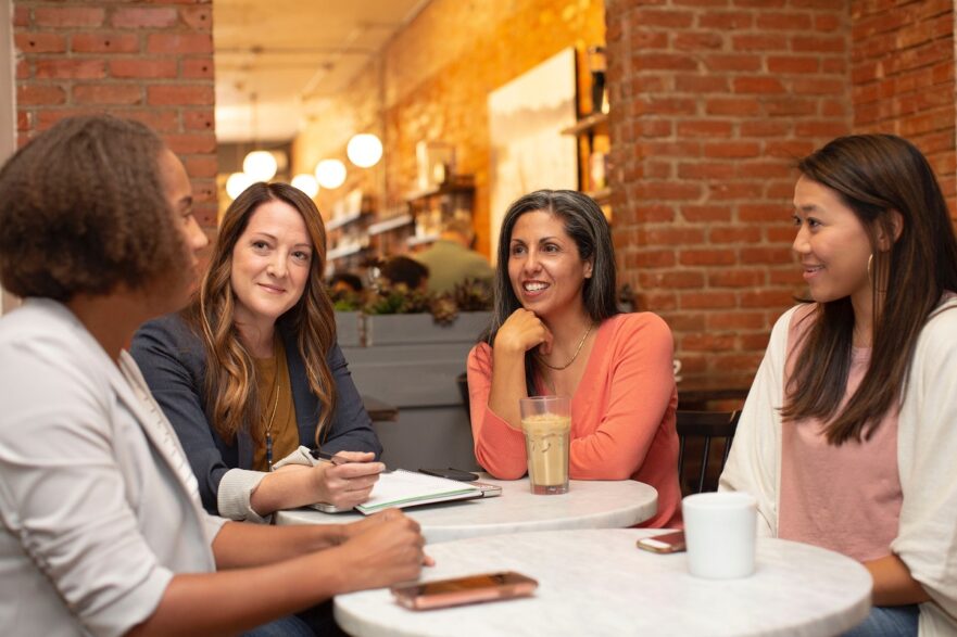 Quatro mulheres participam de uma reunião de trabalho em uma cafeteria