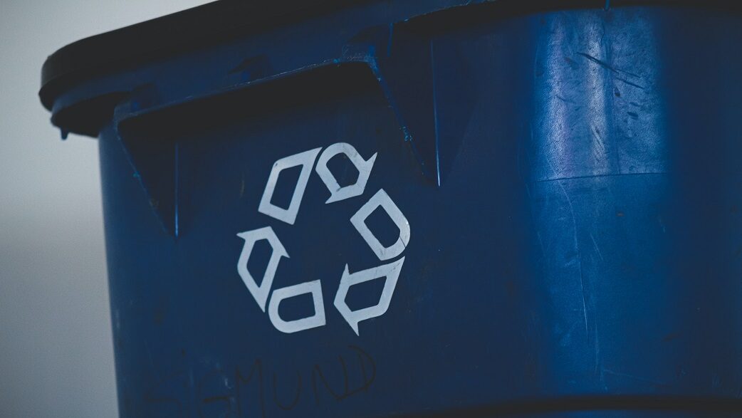 Imagem mostra cesto de lixo azul com o símbolo da reciclagem