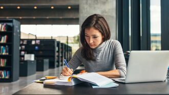 jovem mulher faz anotações a mão em caderno sentada em biblioteca