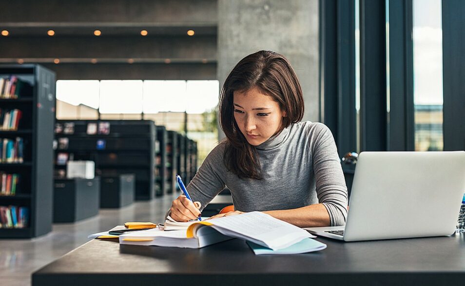 jovem mulher faz anotações a mão em caderno sentada em biblioteca