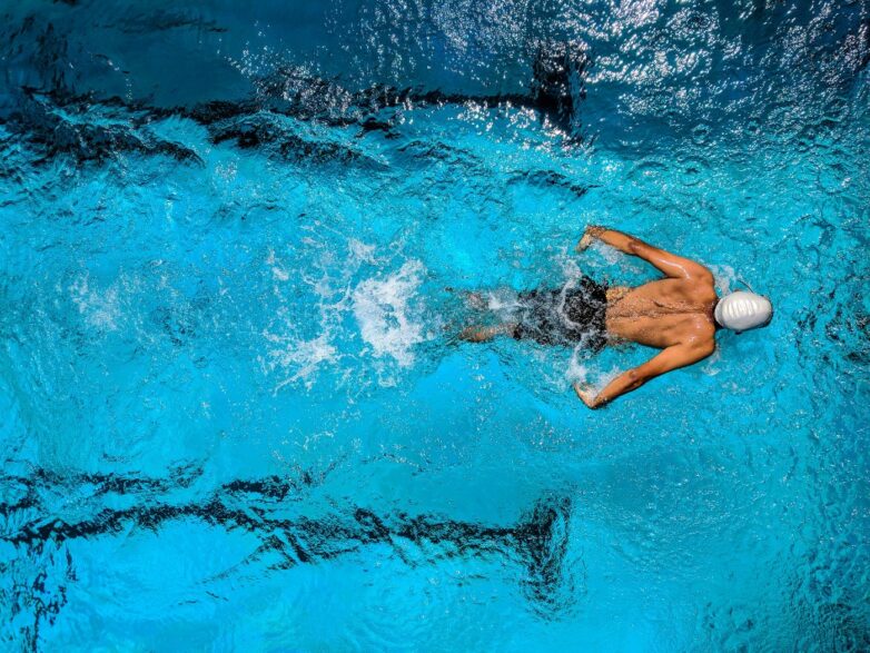 homem de touca nadando em piscina bem azul