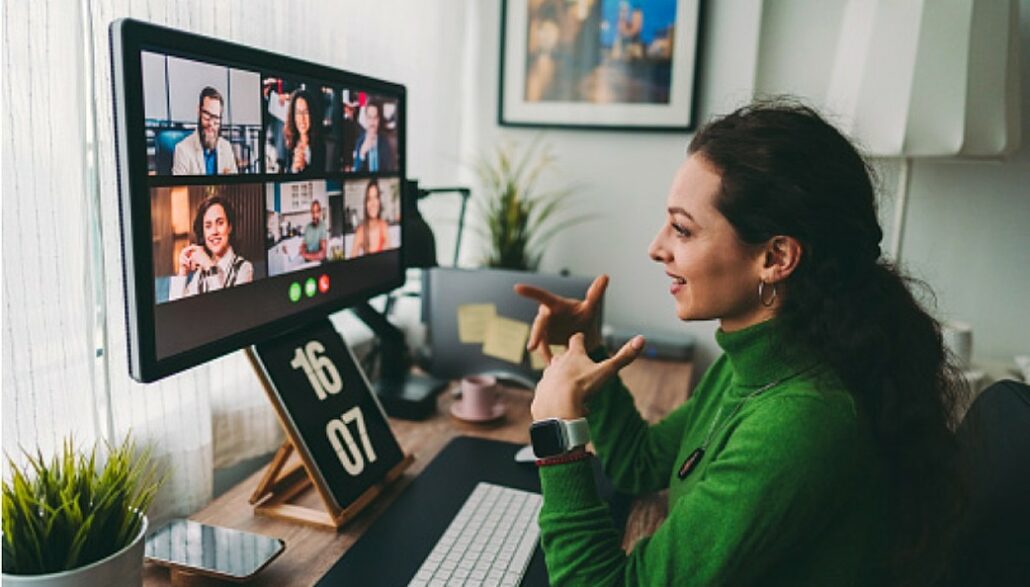 mulher com blusa verde sentada à frente do desktop participa de reunião online do trabalho
