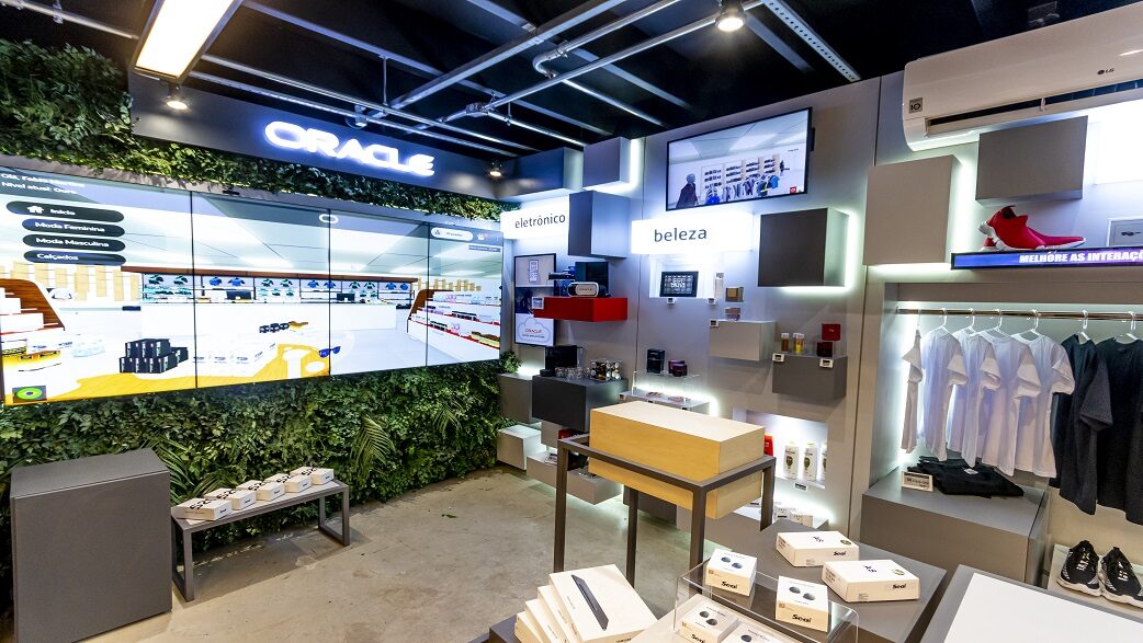 Imagem mostra a loja conceito da Oracla, com prateleiras brancas iluminadas e um telão.