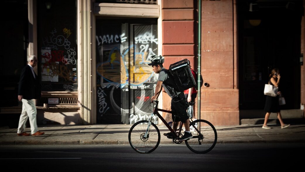 Imagem mostra um homem com uma mochila térmica nas costas andando de bicicleta