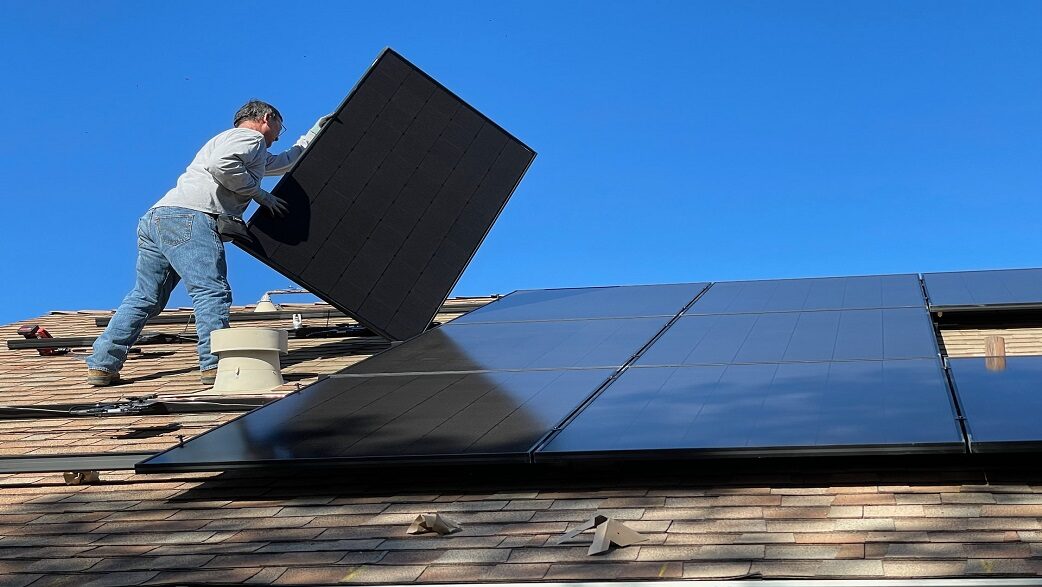 Imagem mostra um homem instalando placas de energia solar em um telhado