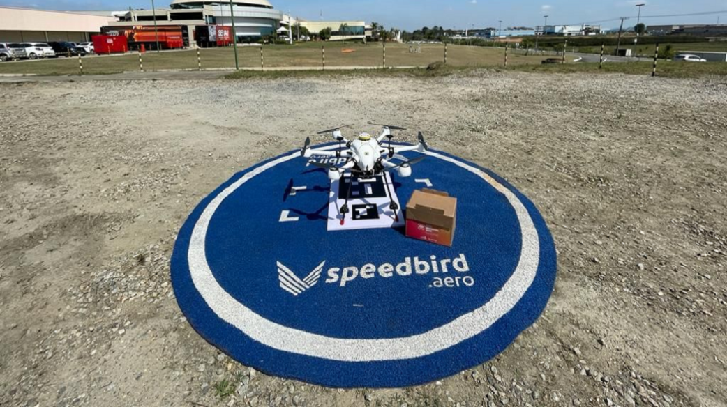 Imagem mostra um drone pousado no chão ao lado de uma caixa de papel.