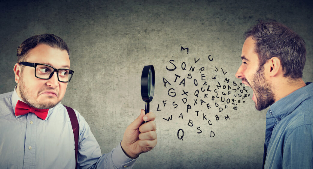 Curious businessman looking through a magnifying glass at an angry screaming man